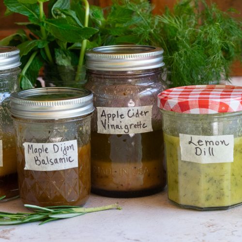 homemade vinaigrettes on a gray counter top with fresh herbs in the back ground