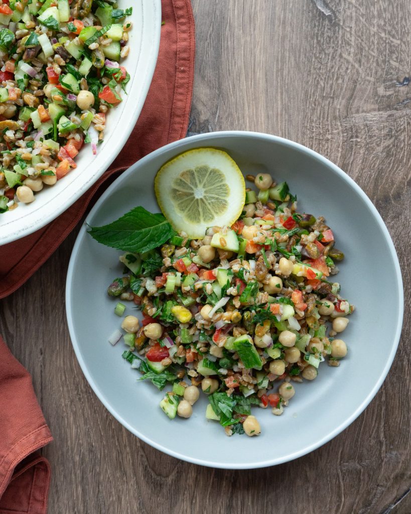 side dish of farro salad next to a larger serving dish full of the salad on a wood counter top