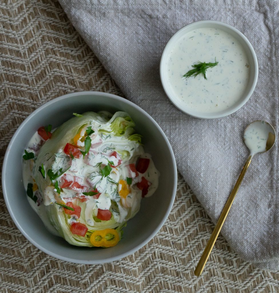 wedge salad in a gray bowl topped with peppers, tomatoes, and buttermilk ranch dressing. pint jar with buttermilk ranch dressing in upper right hand corner of picture