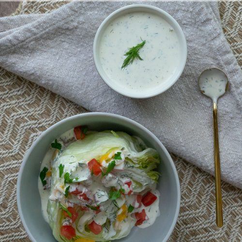 wedge salad in a gray bowl with buttermilk ranch dressing small bowl of ranch dressing in upper right hand corner a gold spoon is laying off to the right of the bowl