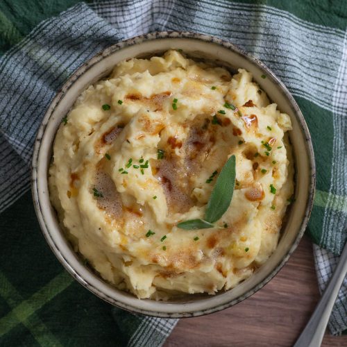 Bowl of mashed potatoes garnished with sage and drizzled with brown butter