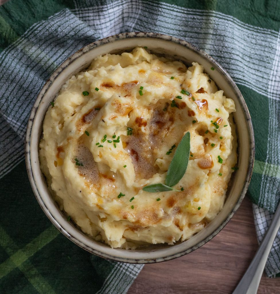 Bowl of mashed potatoes garnished with sage and drizzled with brown butter