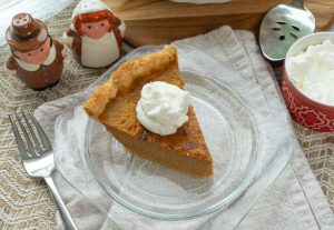 slice of pumpkin pie with dollop of whipped cream on a glass plate with, table is set for dessert