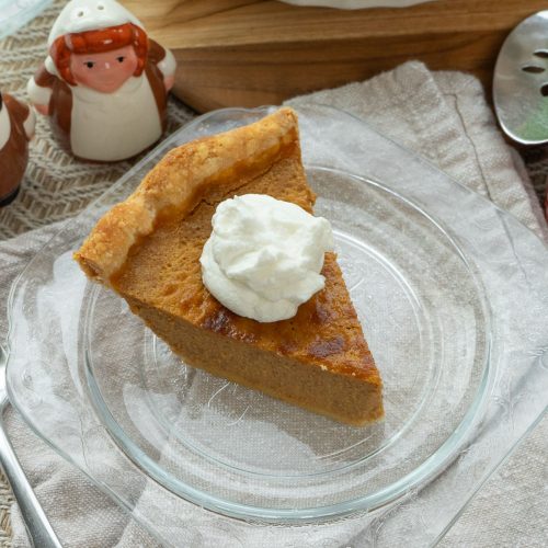 slice of pumpkin pie with dollop of whipped cream on a glass plate with, table is set for dessert