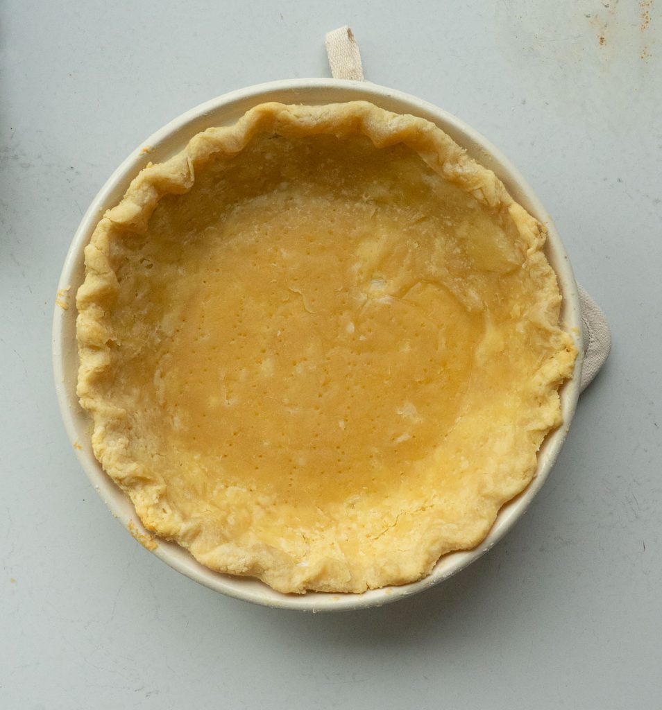 fully baked pie crust in a cream colored pie plate on a gray countertop