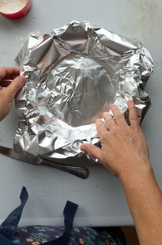 placing foil down into pie plate, on top of uncooked pie dough