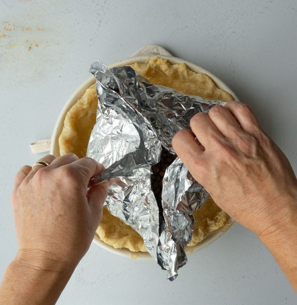 lifting foil with dried beans in it out of the pie crust